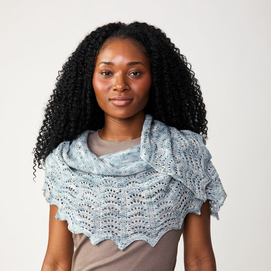 Woman wearing a light blue knitted shawl over a brown shirt against a plain background